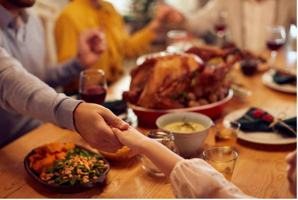 A group of people eating thanksgiving dinner, holding hands