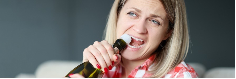 Person biting off the cork on a bottle