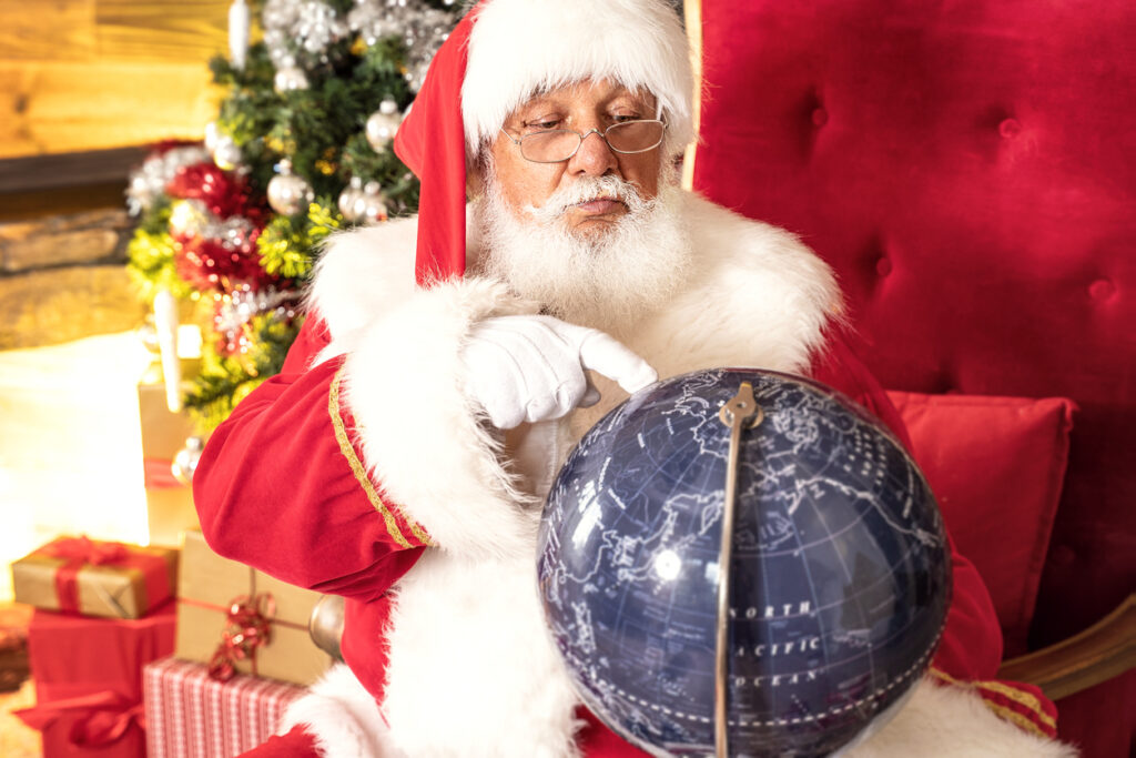 Real Santa Claus Sitting Near Christmas Tree and looking at the globe. Braces-Friendly Holiday Treats: Holiday Fun from Around the World