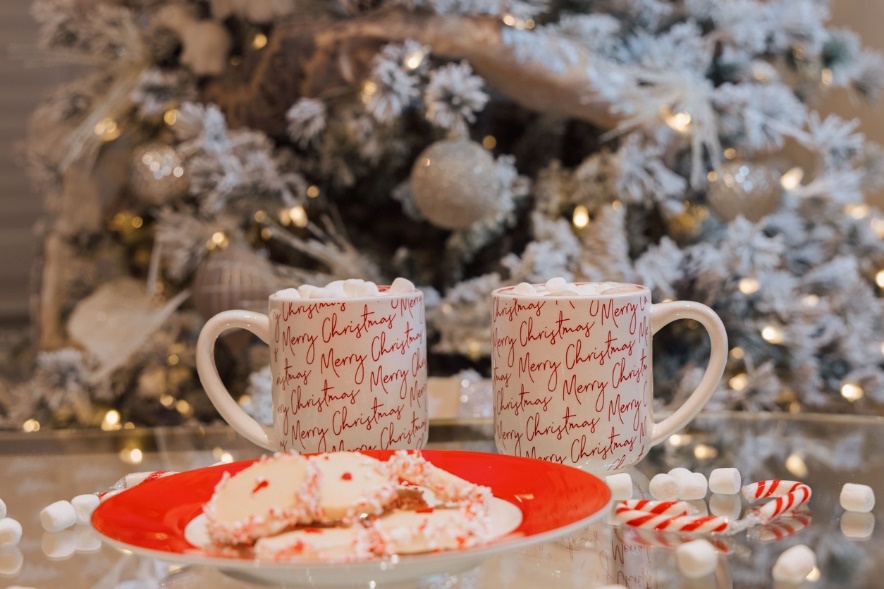 Two mugs with marshmallows and a plate of cookies