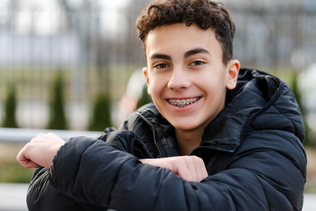 Portrait of positive happy boy, handsome teenager with braces looking at camera, wearing casual outfit standing on urban street. Advertisement concept, dental care, Achieve Your Best Smile: Setting Orthodontic Goals for 2025